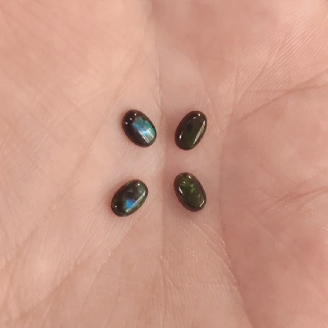 Four lab grown ovals opals black with green fire In a hand.