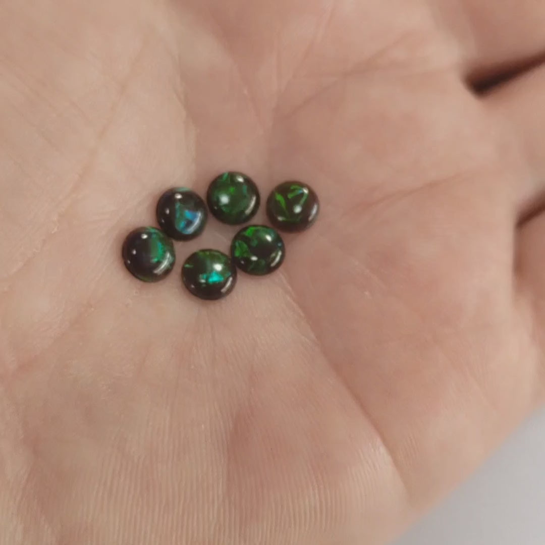Six round fireable cabochon opal gemstone In vibrant green and blue flashes, displayed on a hand.