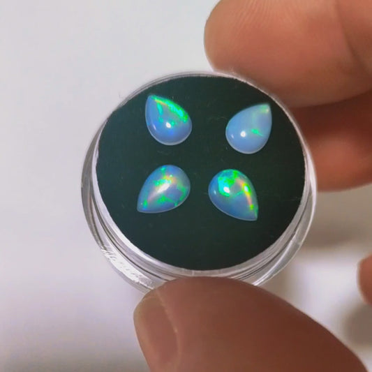 Four lab grown fireable opals, white with green flashes displayed on a gem box with a hand showing the green flashes.