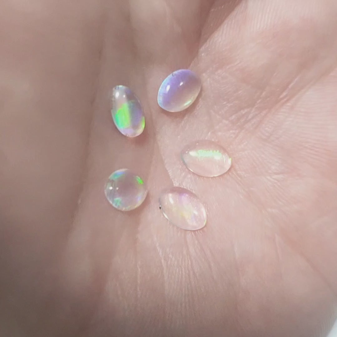 Five water opals with green fire marquise cabochons, displayed on a hand to show green flashes.