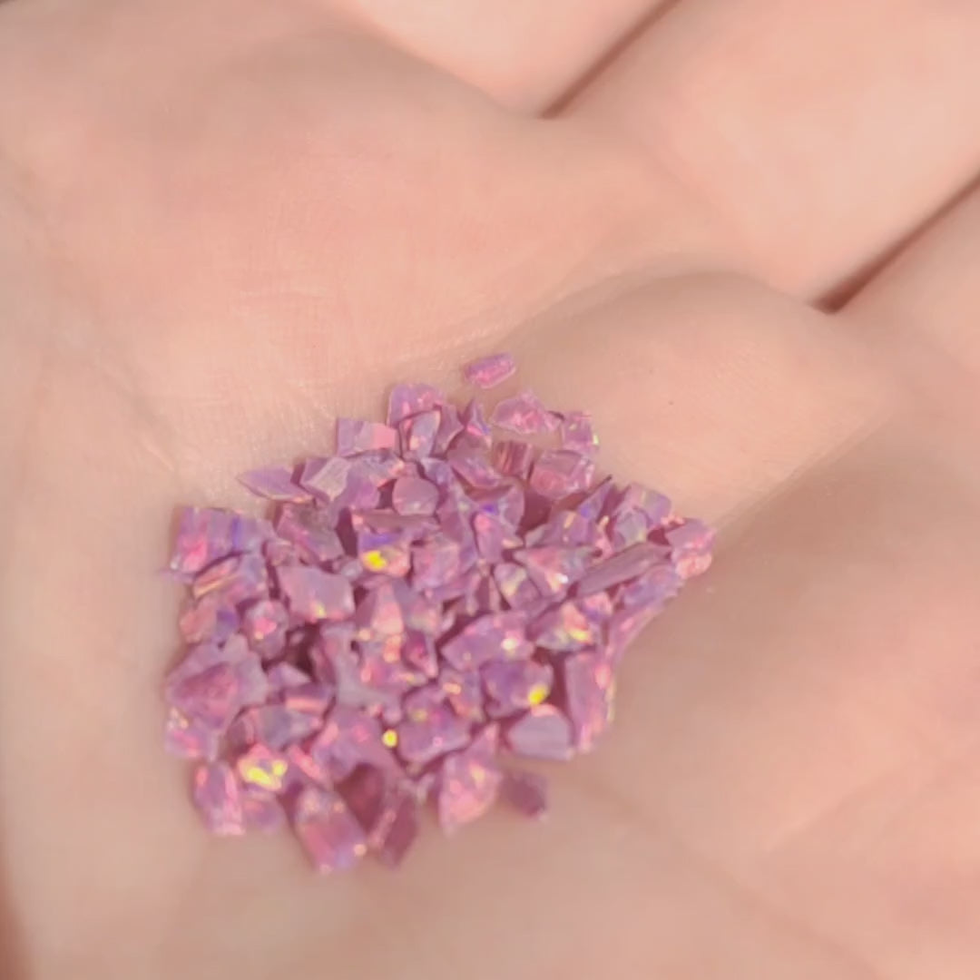 A small handful of resin impregnated lab grown opal chips. Raspberry purple colour with gold, pink and green flashes held in a hand.