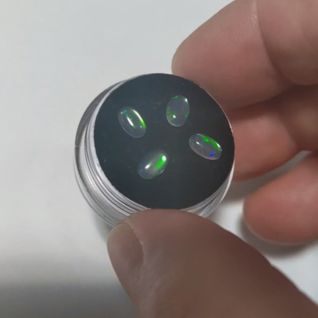 Four oval lab grown water opals with green fire held in a hand showing the green flashes.