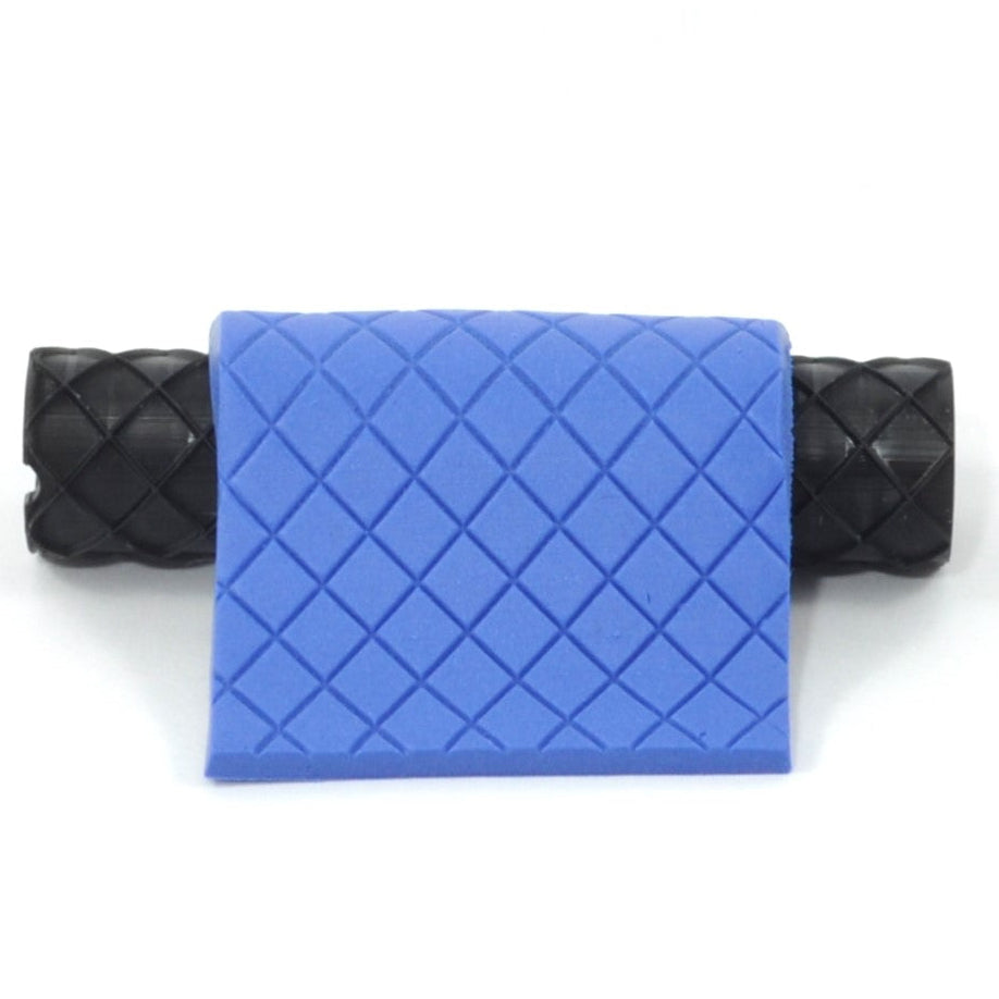 Blue quilted polymer clay design with black textured roller on a white background