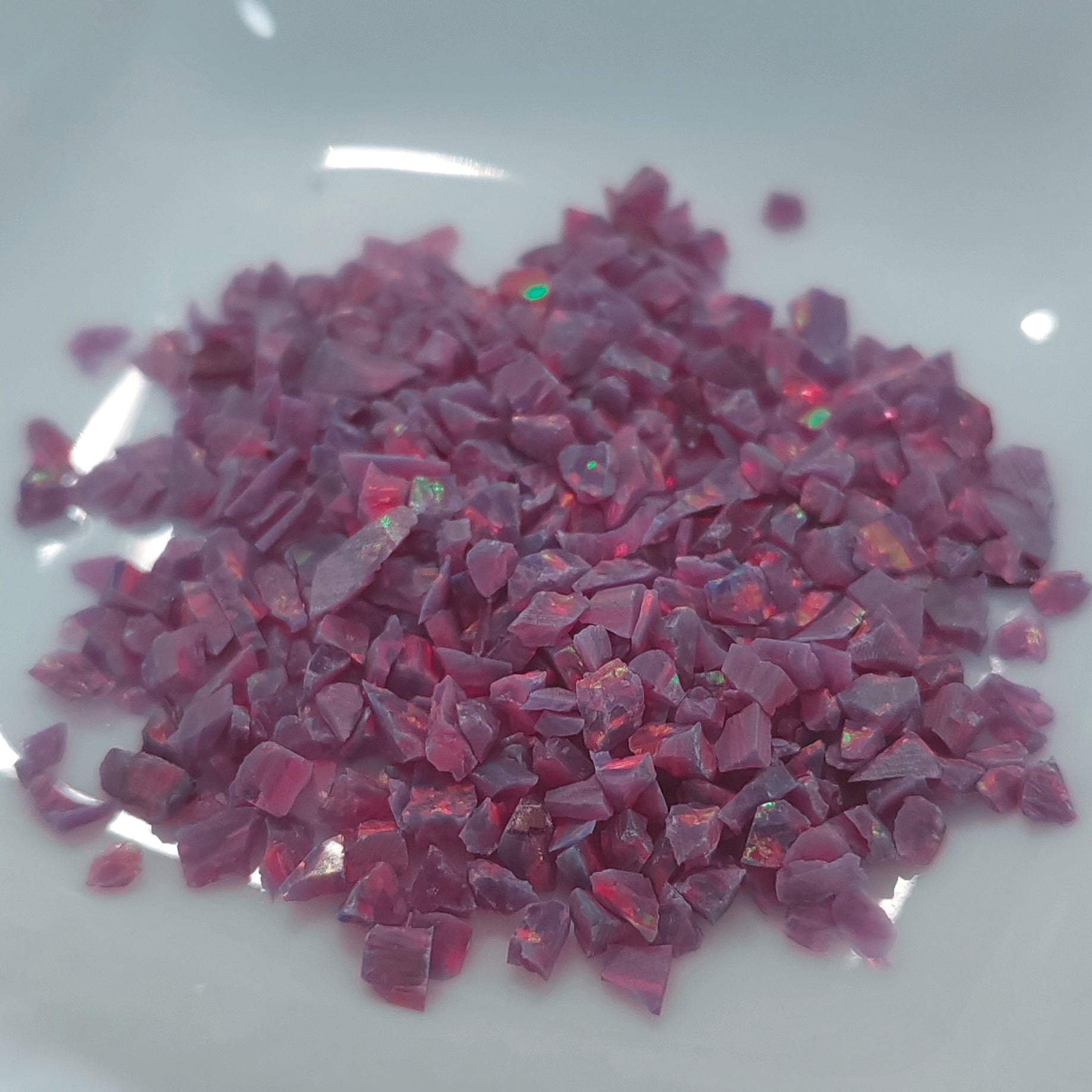 A pile of small, purple-pink opal chips with an iridescent, opalescent sheen, resting on a white surface.