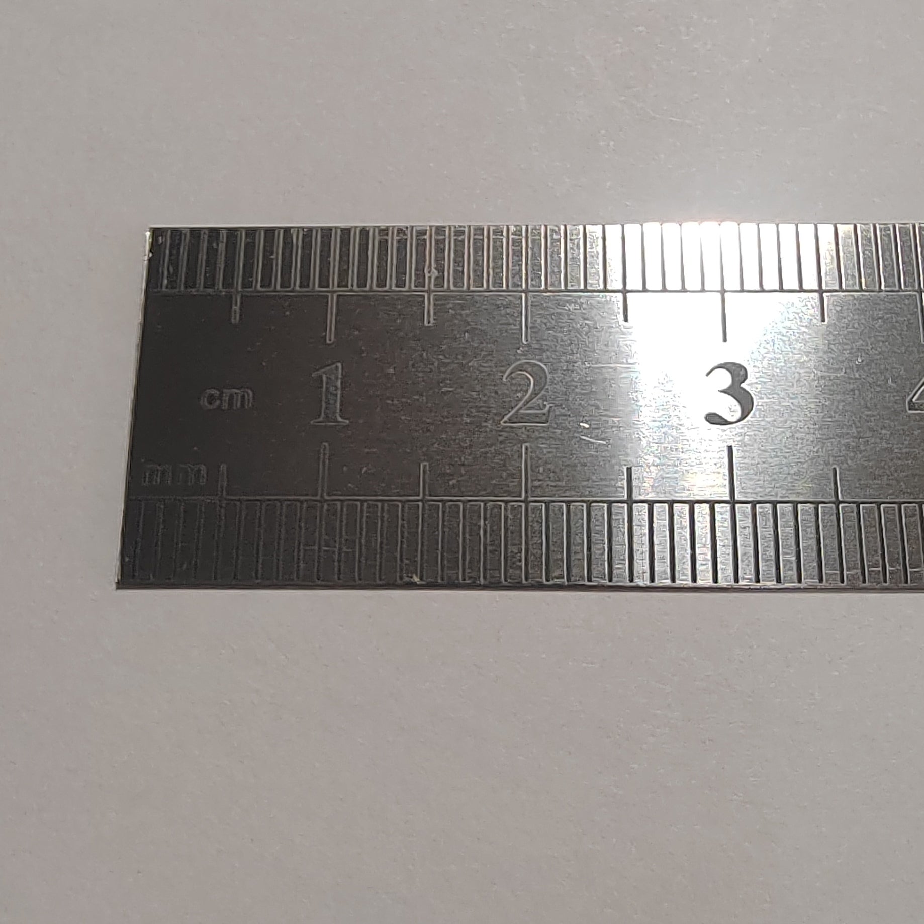A stainless steel ruler with centimeter and millimeter markings, shown horizontally against a plain light grey background.