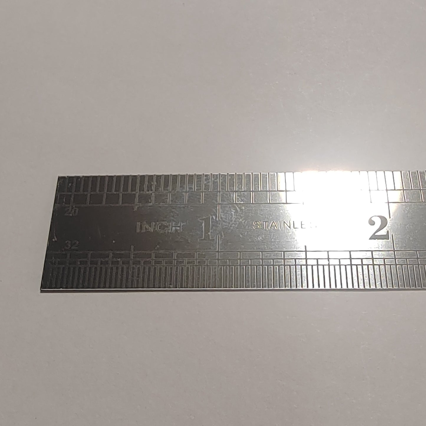 A stainless steel ruler with inch and centimetre markings, photographed on a plain light grey background.