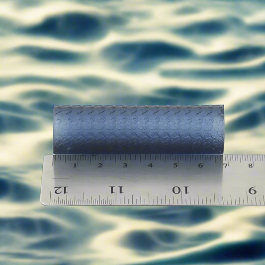 A textured roller tool for crafting, placed on top of a ruler for scale, indicating its use for creating even textured designs in jewelry making.